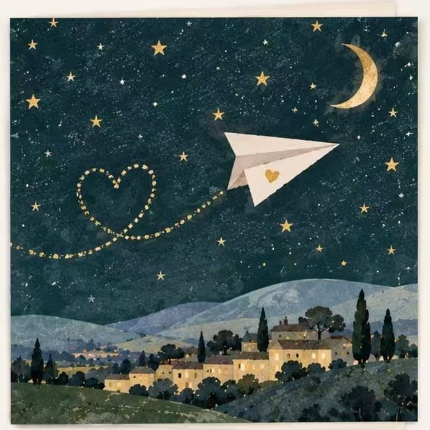 Magical Good Wishes card with a paper airplane leaving a heart-shaped trail over a starry night village. 300gsm premium art card, perfect for long-distance thinking of you.