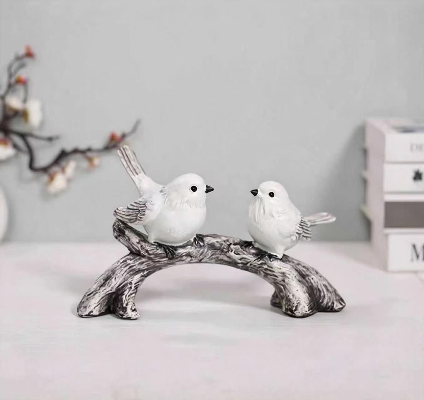 Two white bird figurines facing each other on a curved branch