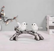 Two white bird figurines facing each other on a curved branch