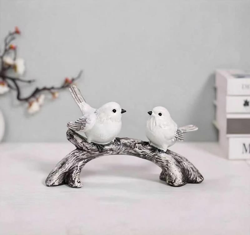 Two white bird figurines facing each other on a curved branch
